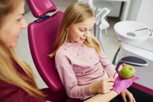 girl learning how to brush her teeth using an apple and a toothbrush