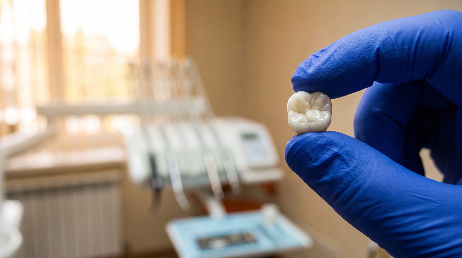 A ceramic dental crown held in a gloved hand