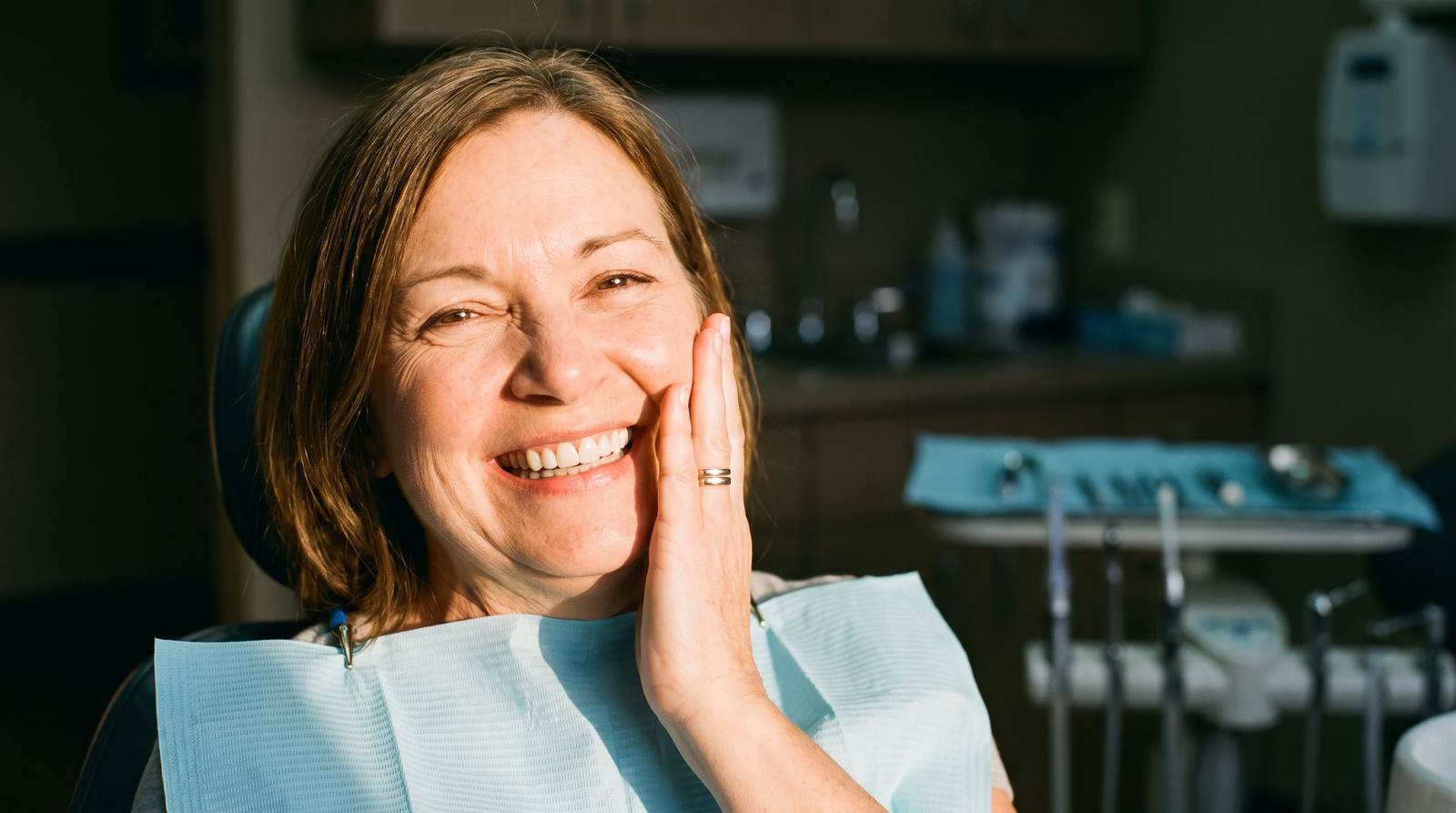 A woman smiling in the dental chair after full mouth restoration